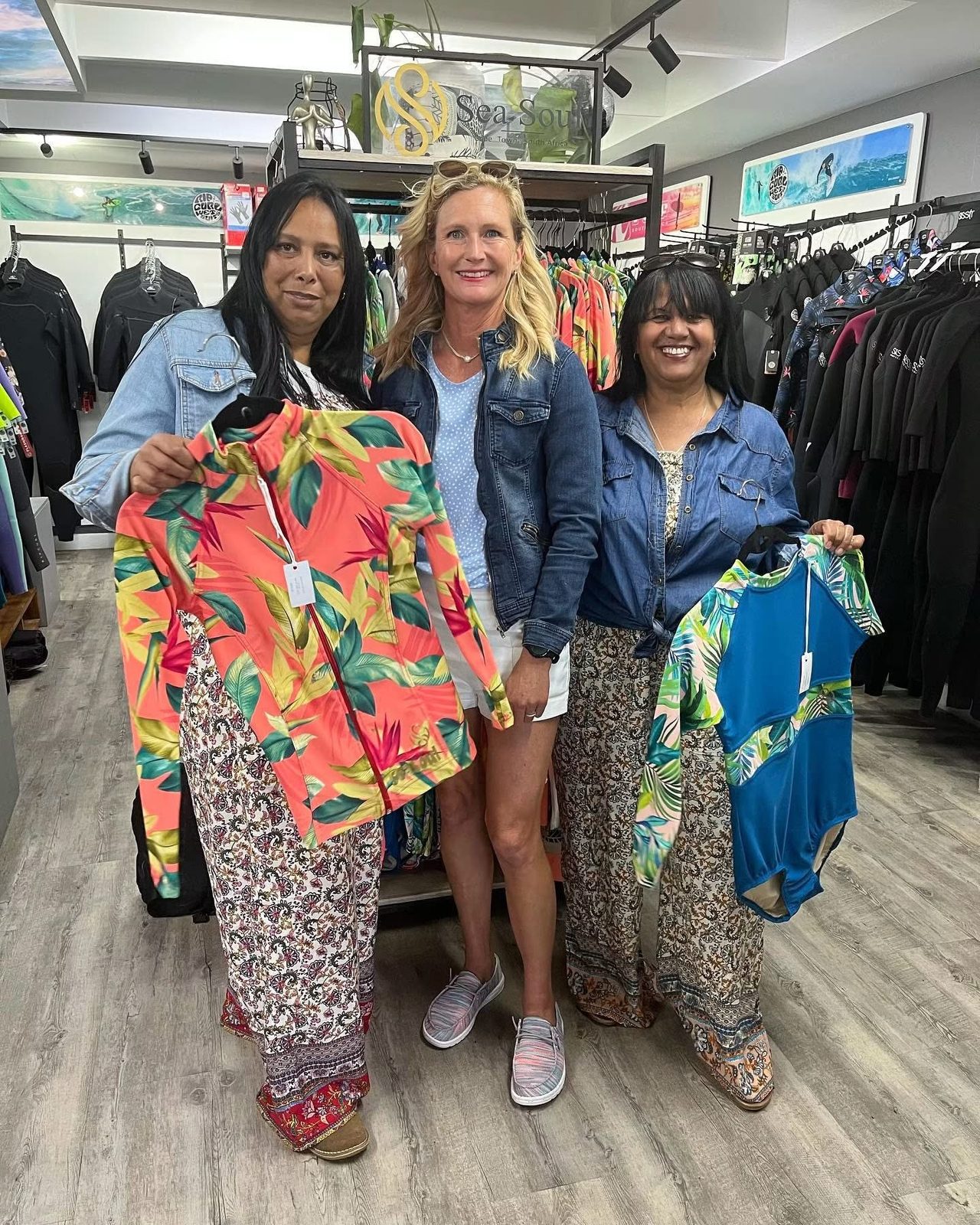 Evette holding Sea Soul rash vests with two women in a surf shop